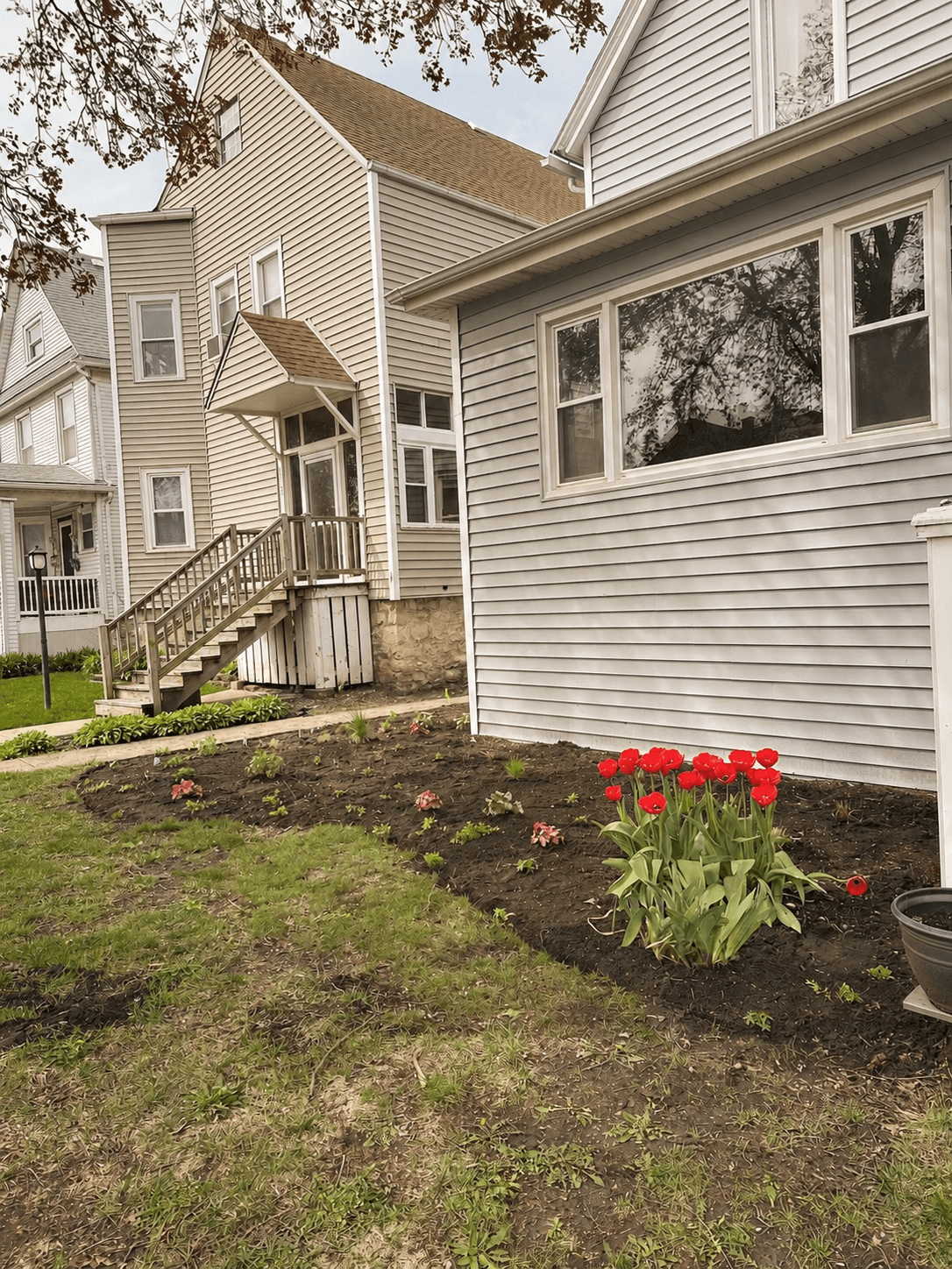 The first layer is in. Young plants, fresh bed lines, and those red tulips holding the drama while the perennials settle in.