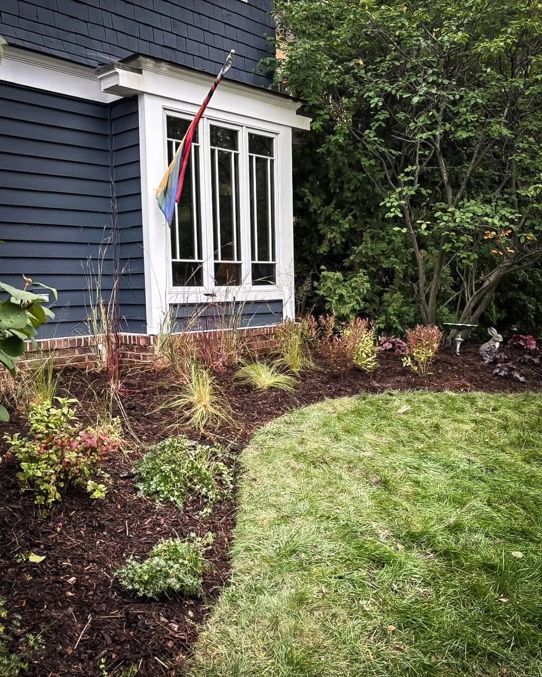 Layered native planting along historic Chicago home foundation with curved garden bed and grasses.