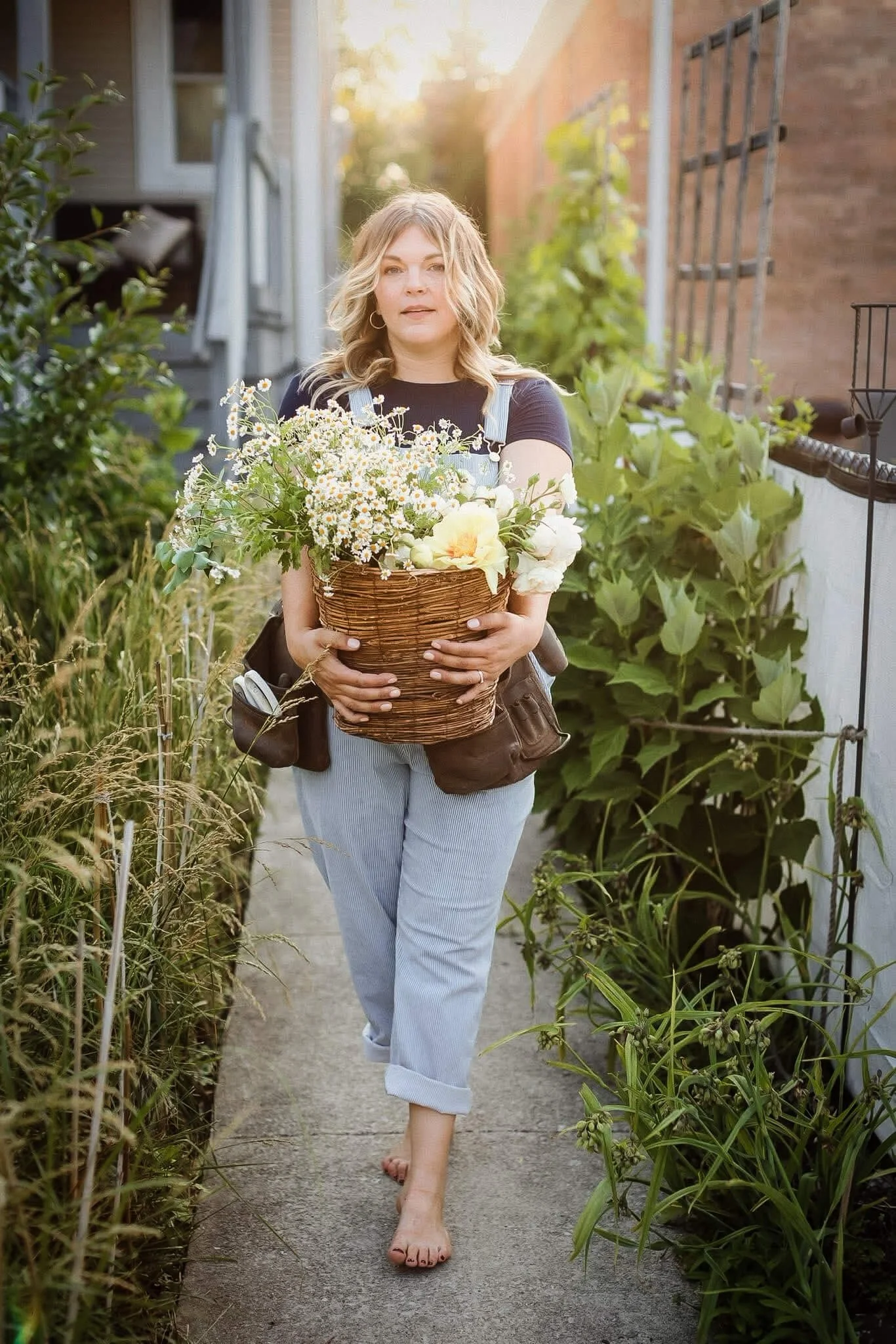 Native Garden Designer holding basket of flowers in garden path.