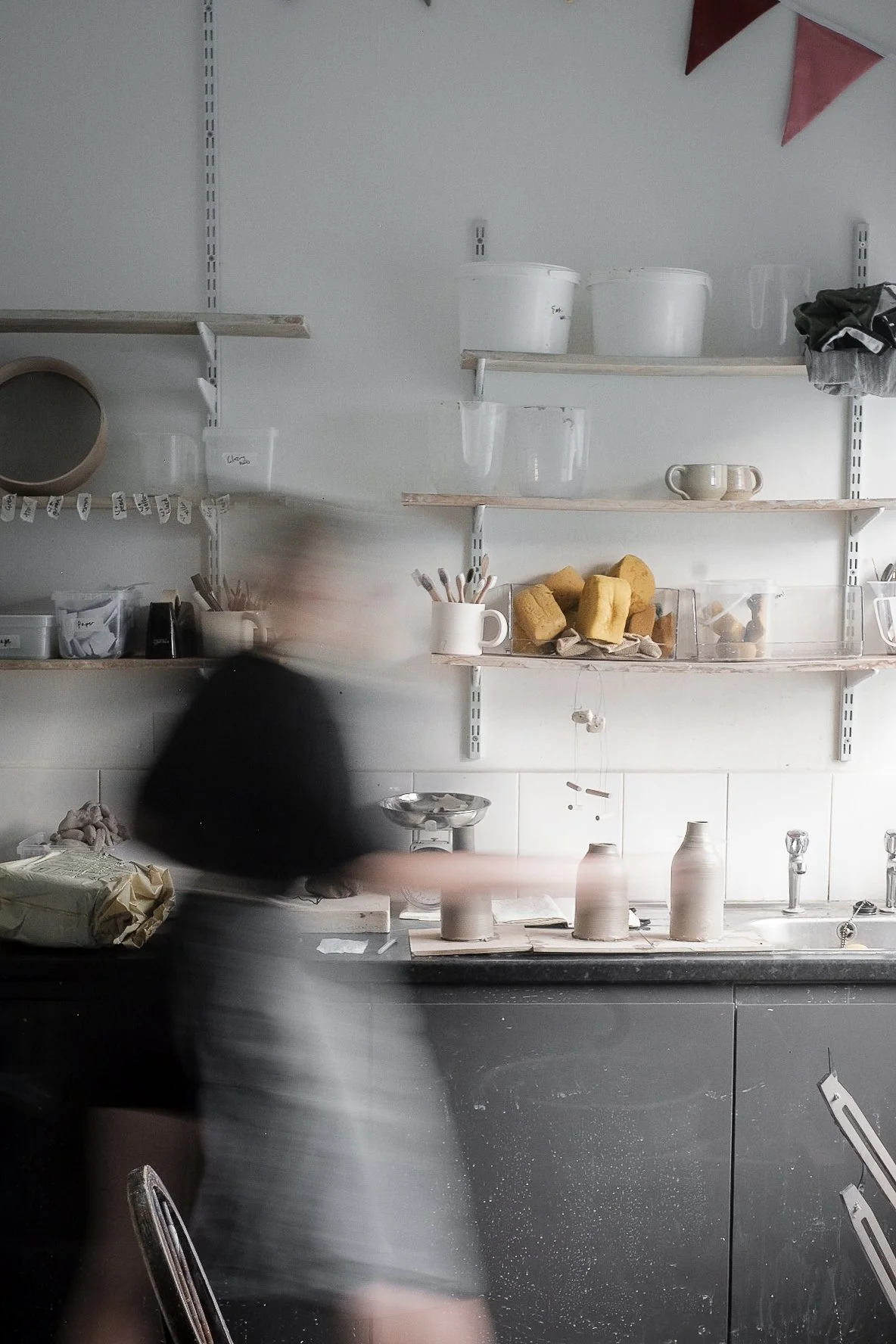 Emma, working at the potters wheel in her Macclesfield pottery studio , with shelves of work in the background
