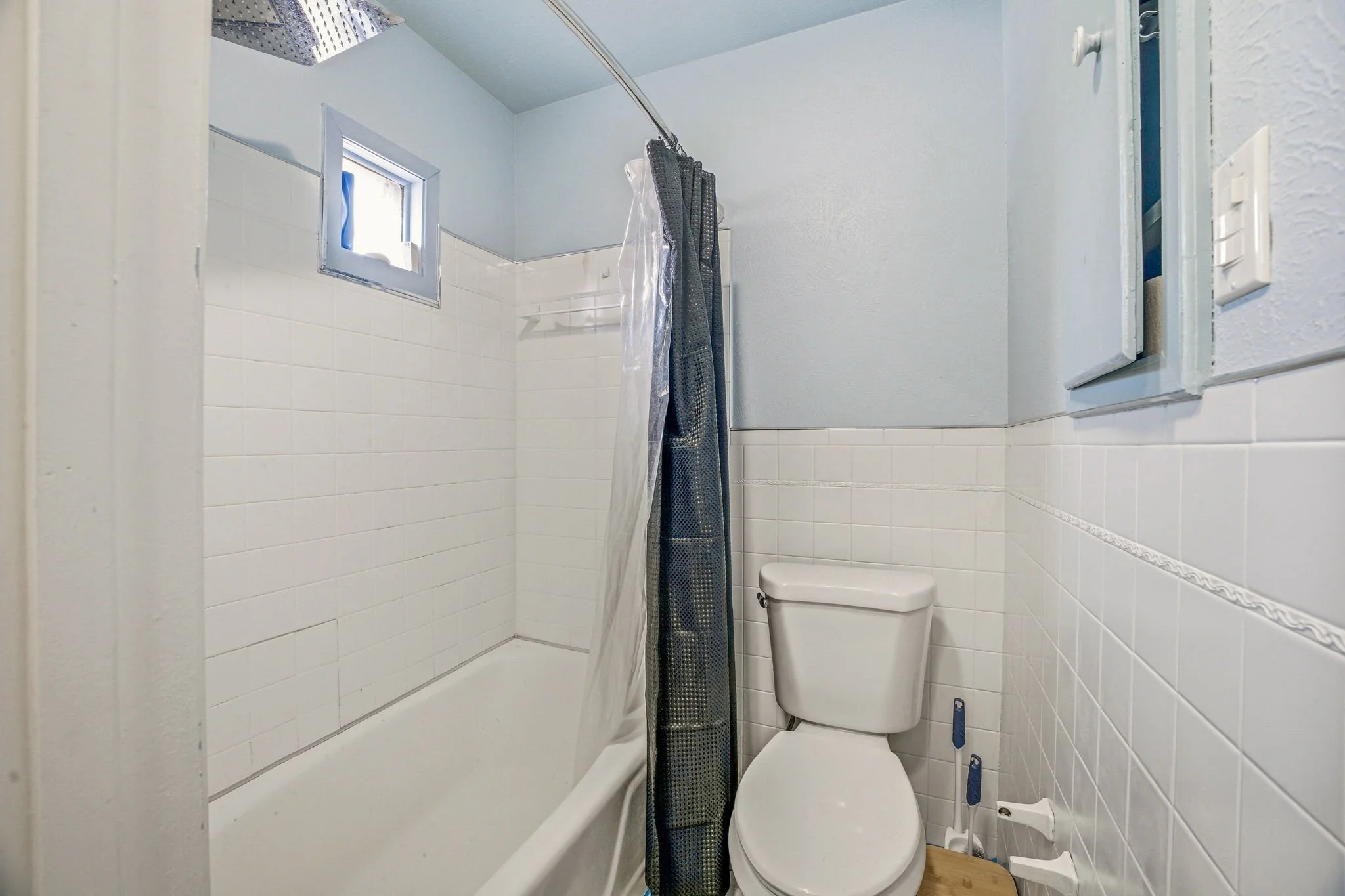 Small bathroom with a bathtub, a toilet, a small window, and a shower curtain