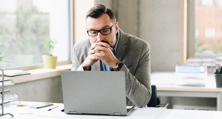 Man sitting in front of a laptop with his fingers interlaced near his face