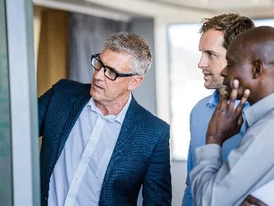 Three men standing and looking at a whiteboard in an office