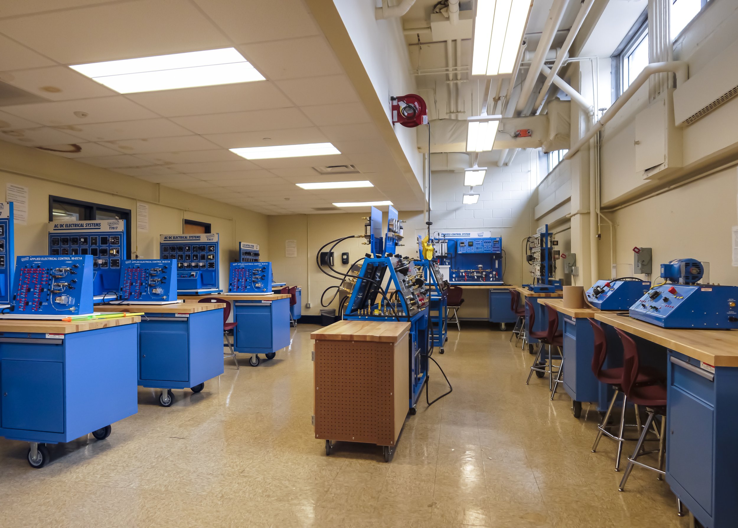 Empty electrical engineering classroom with blue test stations and workbenches, chairs, and technical equipment.