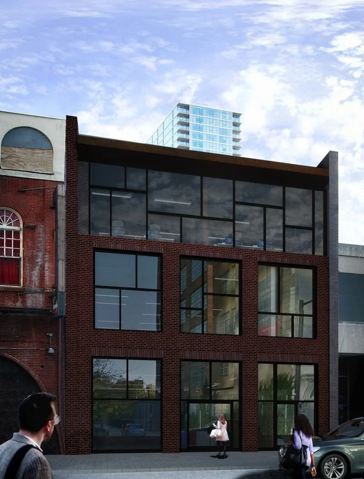 A multi-story brick building with large tinted glass windows on each floor, and a modern glass office space on the top floor, situated on a city street with pedestrians and a parked car in front.