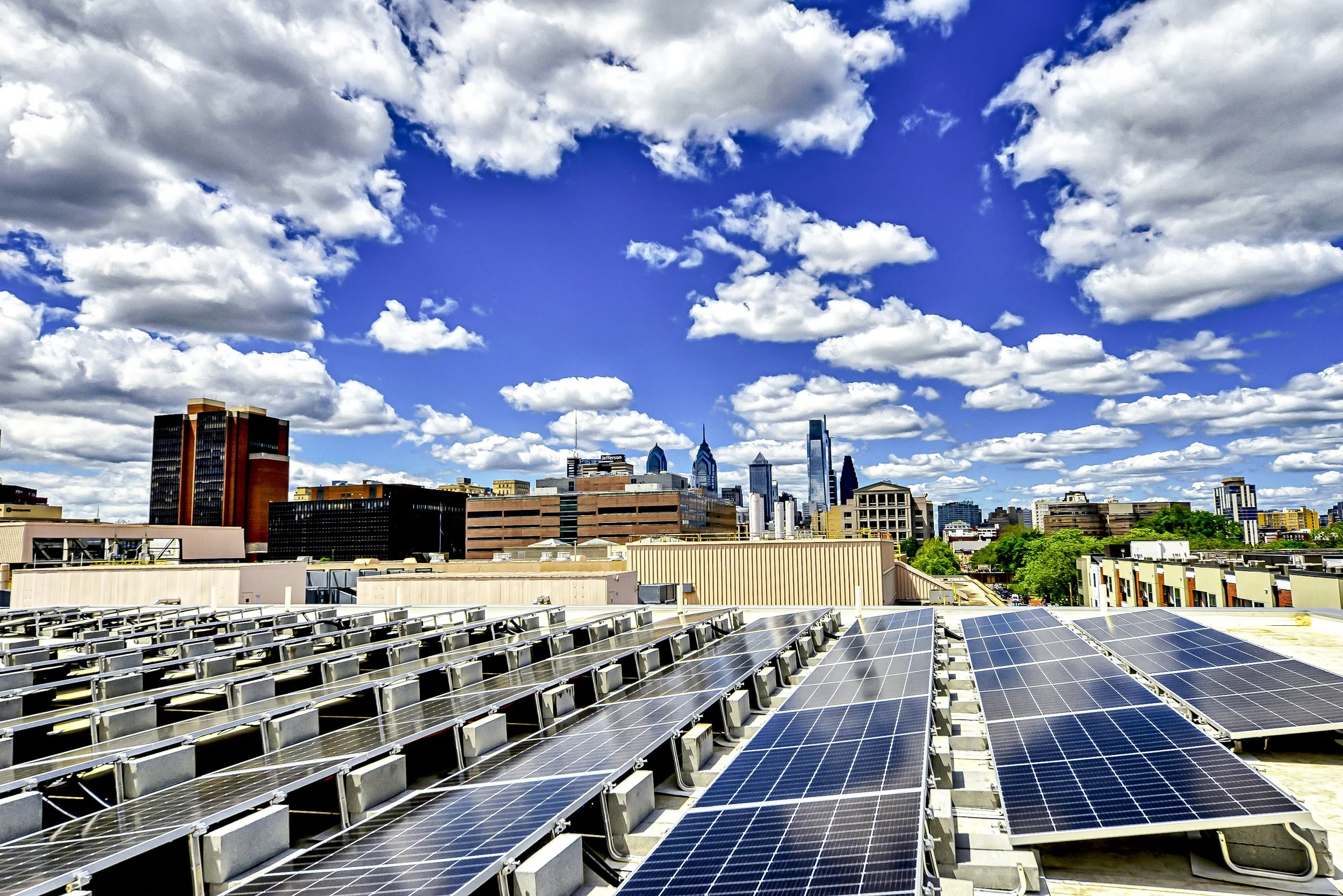 City skyline with tall buildings and a partly cloudy sky, foreground features solar panels on a rooftop.