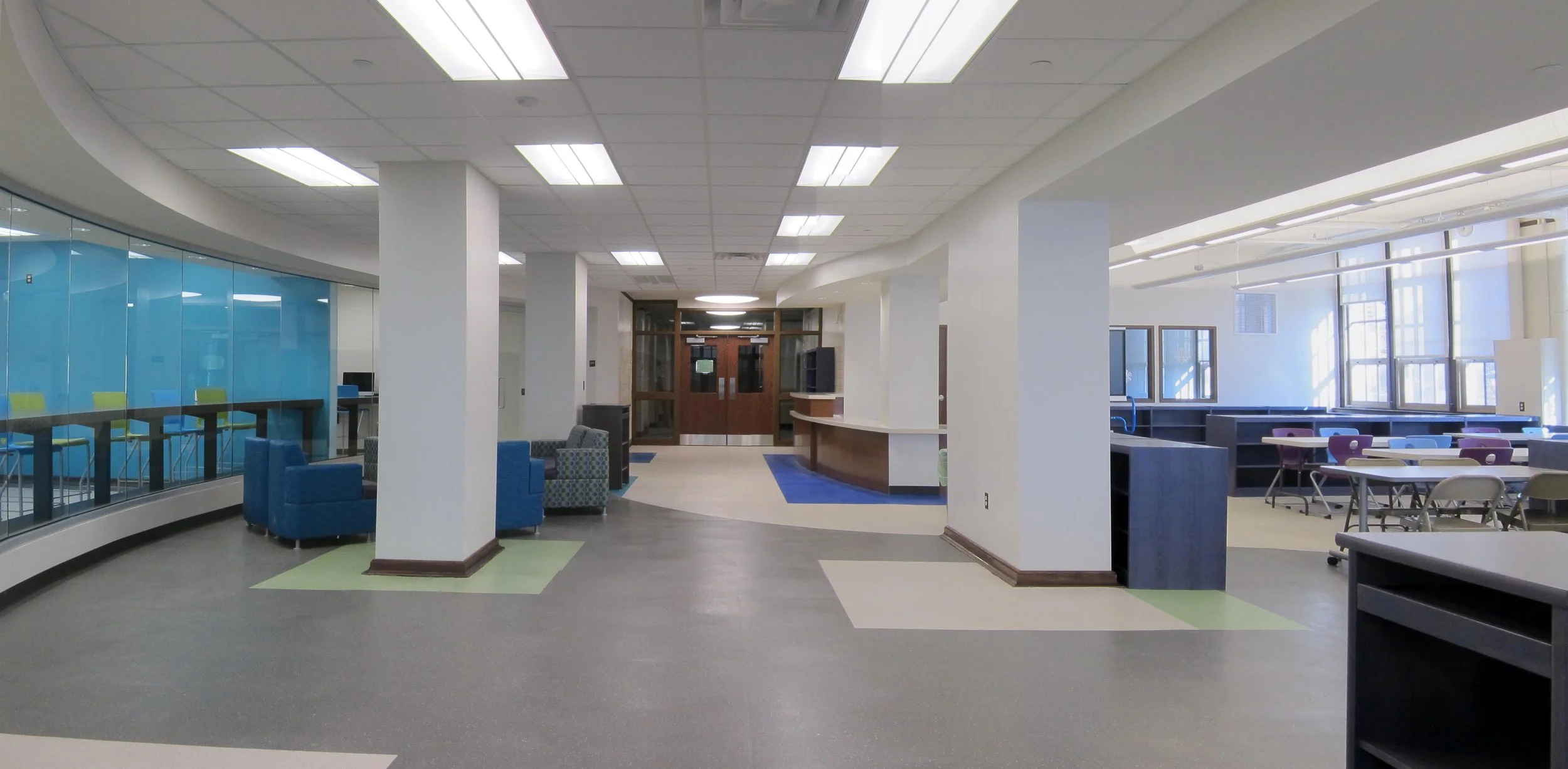 Interior of a modern building lobby with seating areas, a reception desk, and multiple large windows allowing natural light.