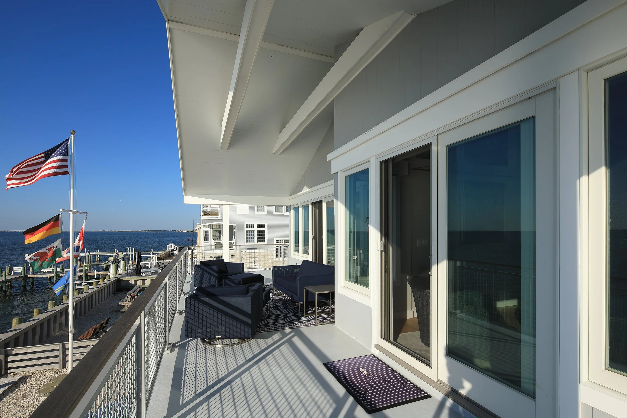Balcony overlooking a body of water with flags, outdoor furniture, and neighboring buildings in the background.