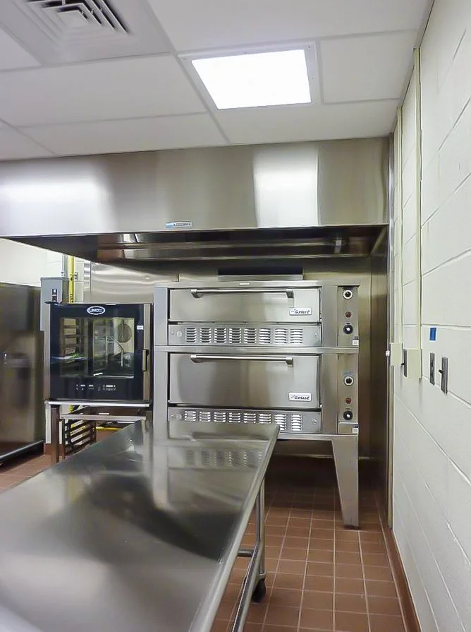 Commercial kitchen with stainless steel appliances, including a double oven, a stainless steel countertop, and a small oven or toaster oven on a cart.