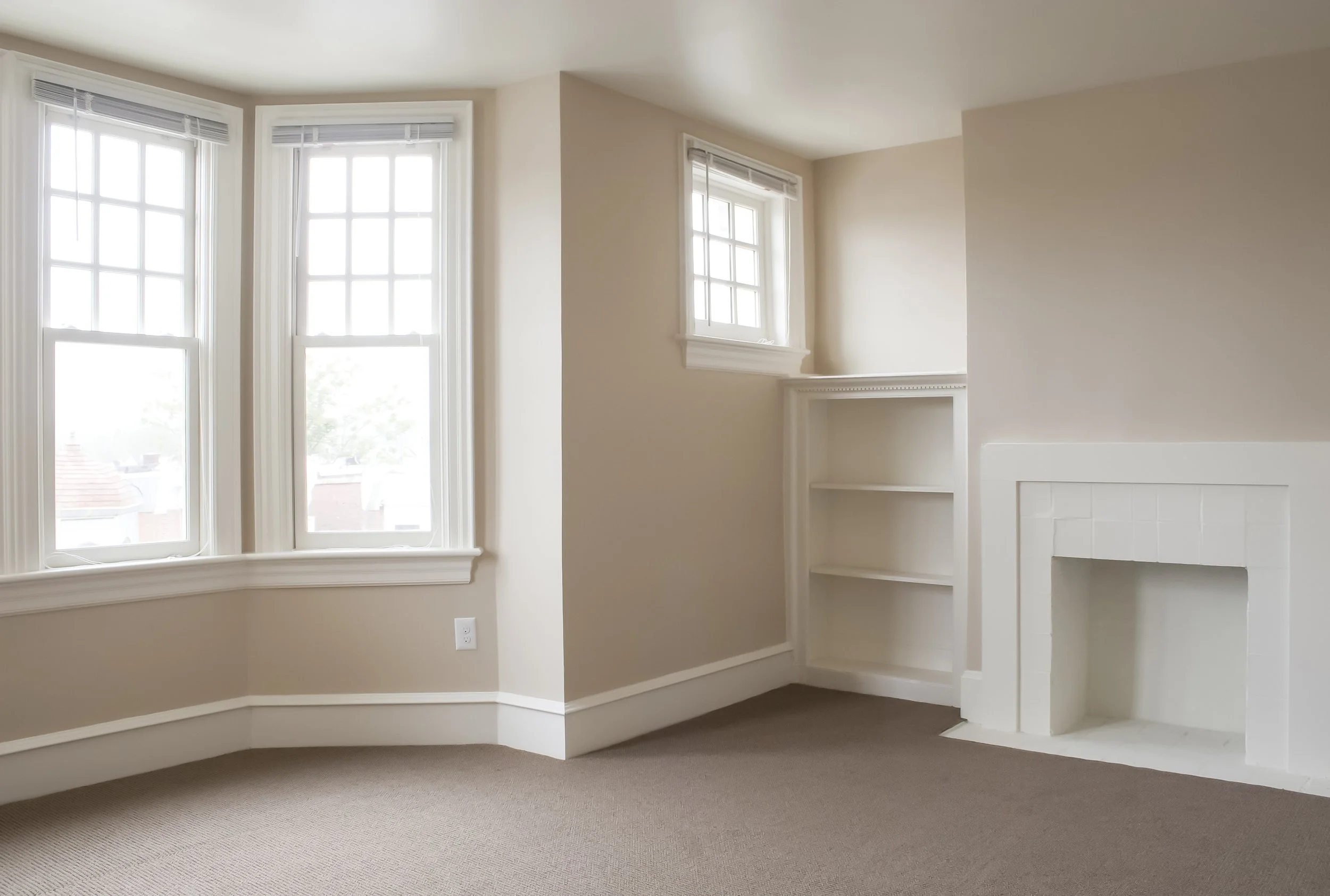 Empty room with three large windows, a fireplace, and built-in white bookshelves.