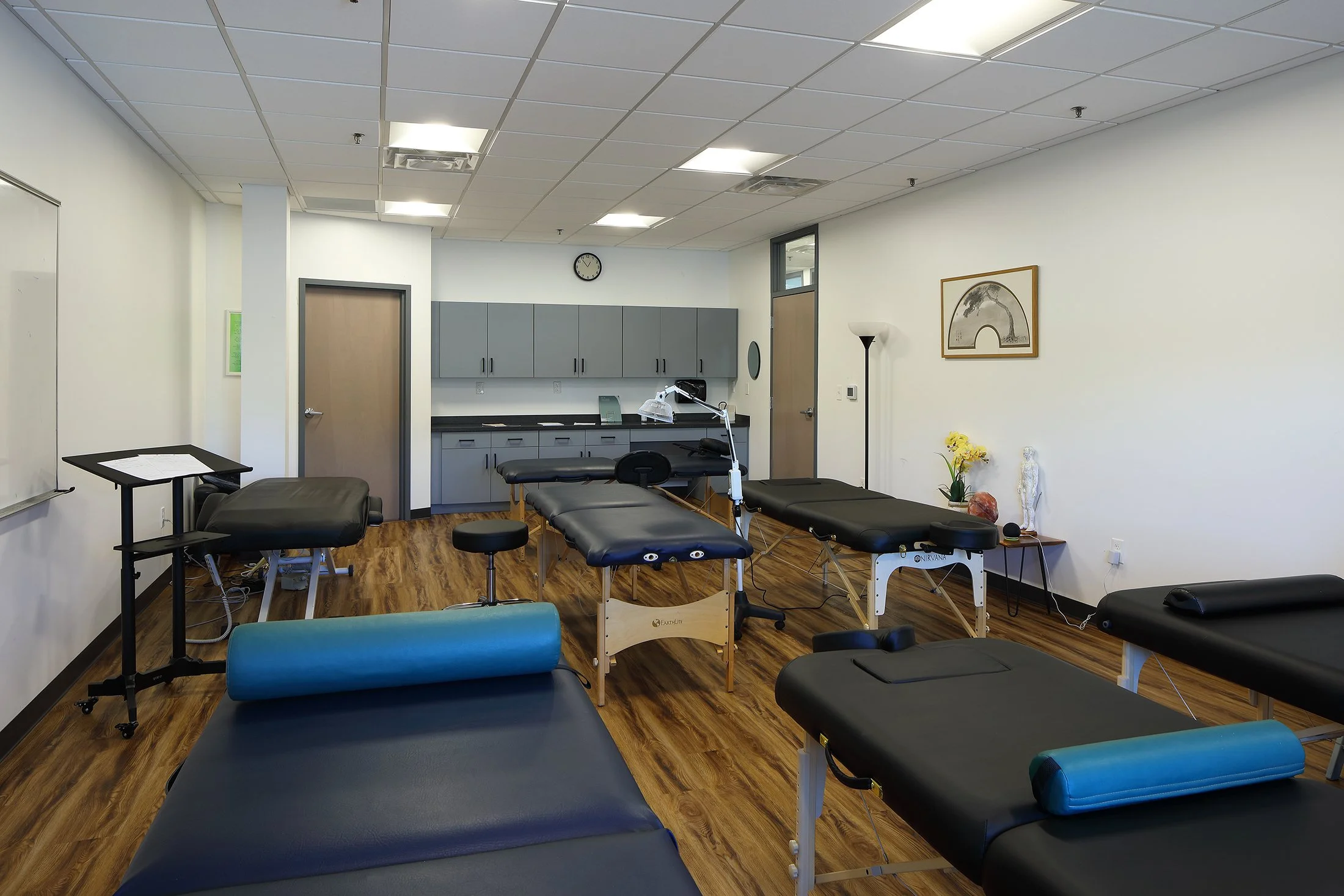 Physical therapy or chiropractor's treatment room with multiple treatment tables, medical equipment, and a whiteboard.