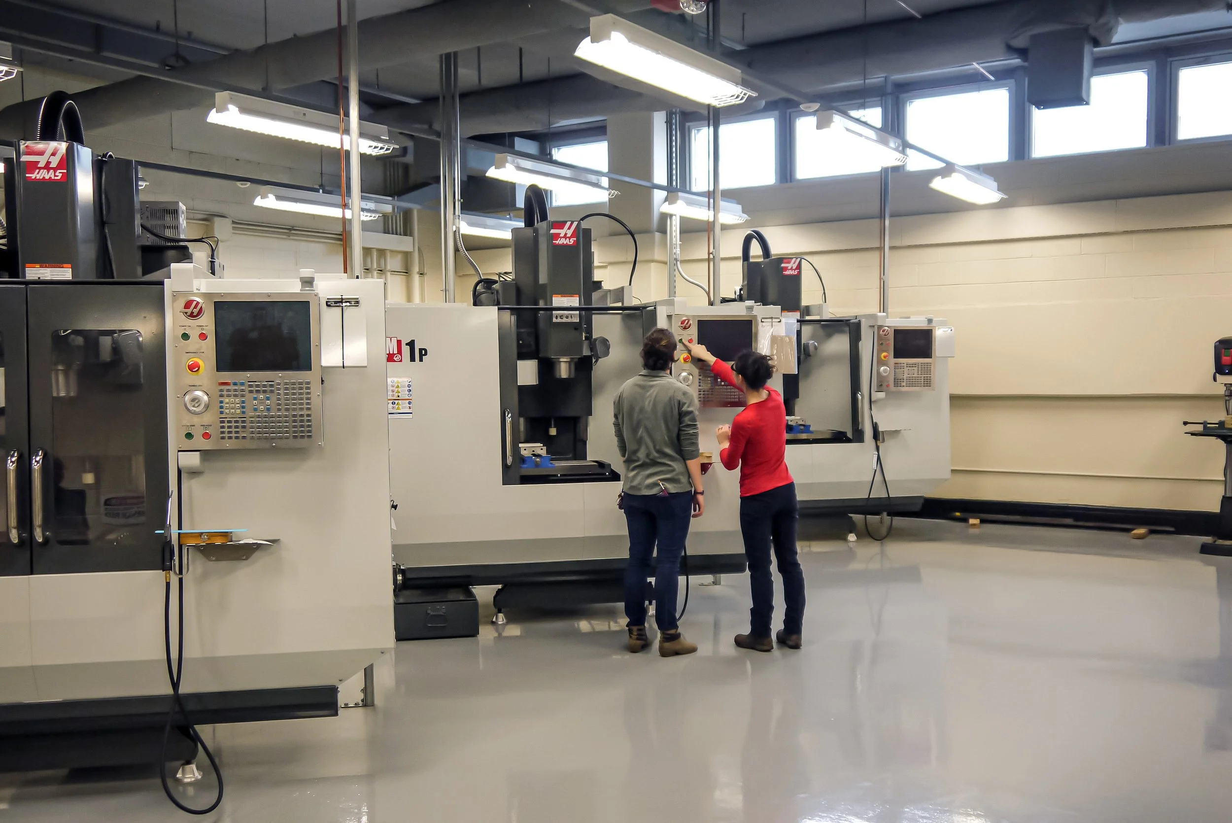 Two women are working with CNC machines in an industrial manufacturing workshop.