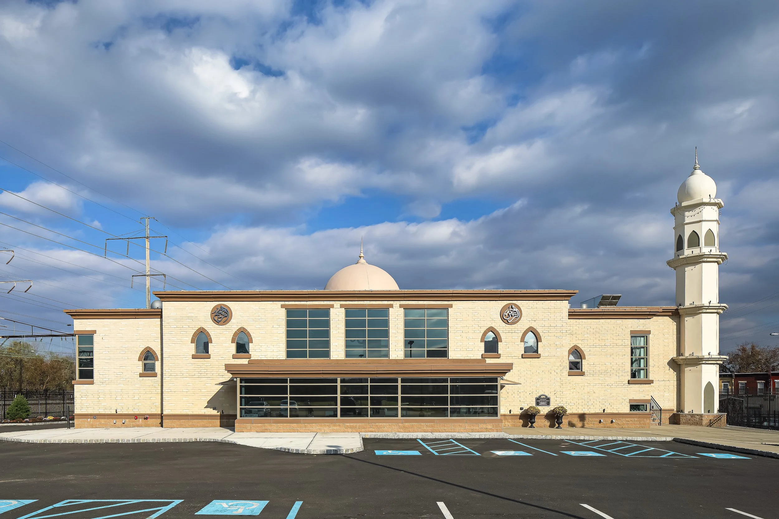 A building resembling a mosque with a large dome and a minaret, against a partly cloudy sky, with a parking lot in front and a few disabled parking spaces.