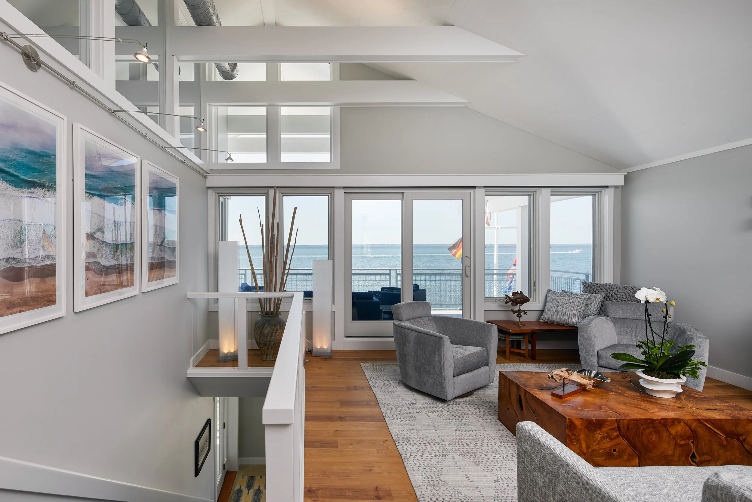 Living room with large glass doors leading to a balcony with ocean view, featuring modern furnishings and wall art.
