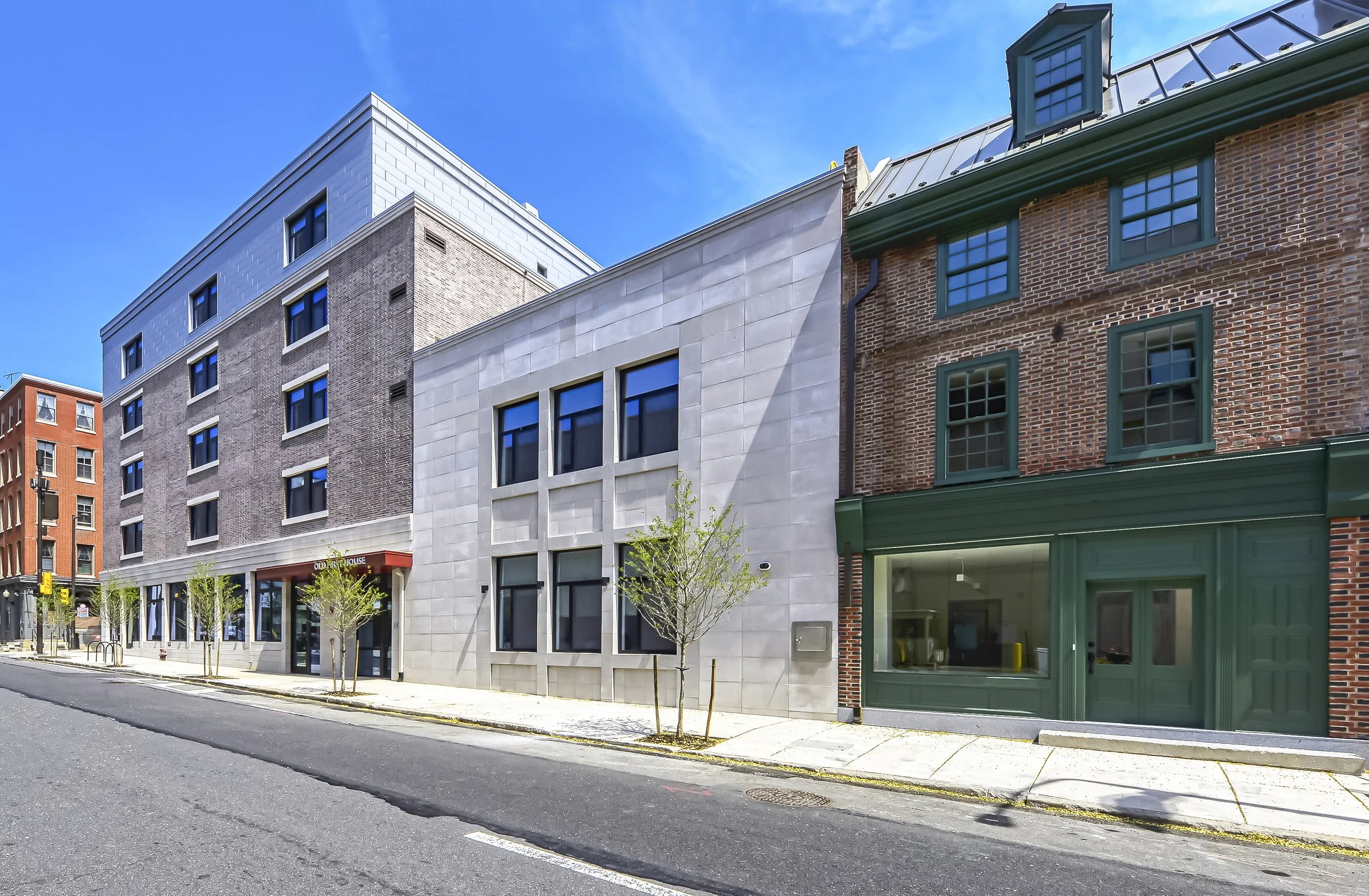 City street with modern and historic buildings, small trees, and clear blue sky.