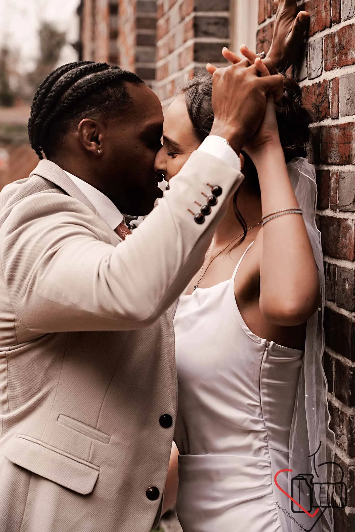 A couple is engaged in a romantic embrace against a brick wall, their faces close and eyes closed, with hands intertwined and pressed against each other's heads. Portsmouth Register Office, Milldam House.