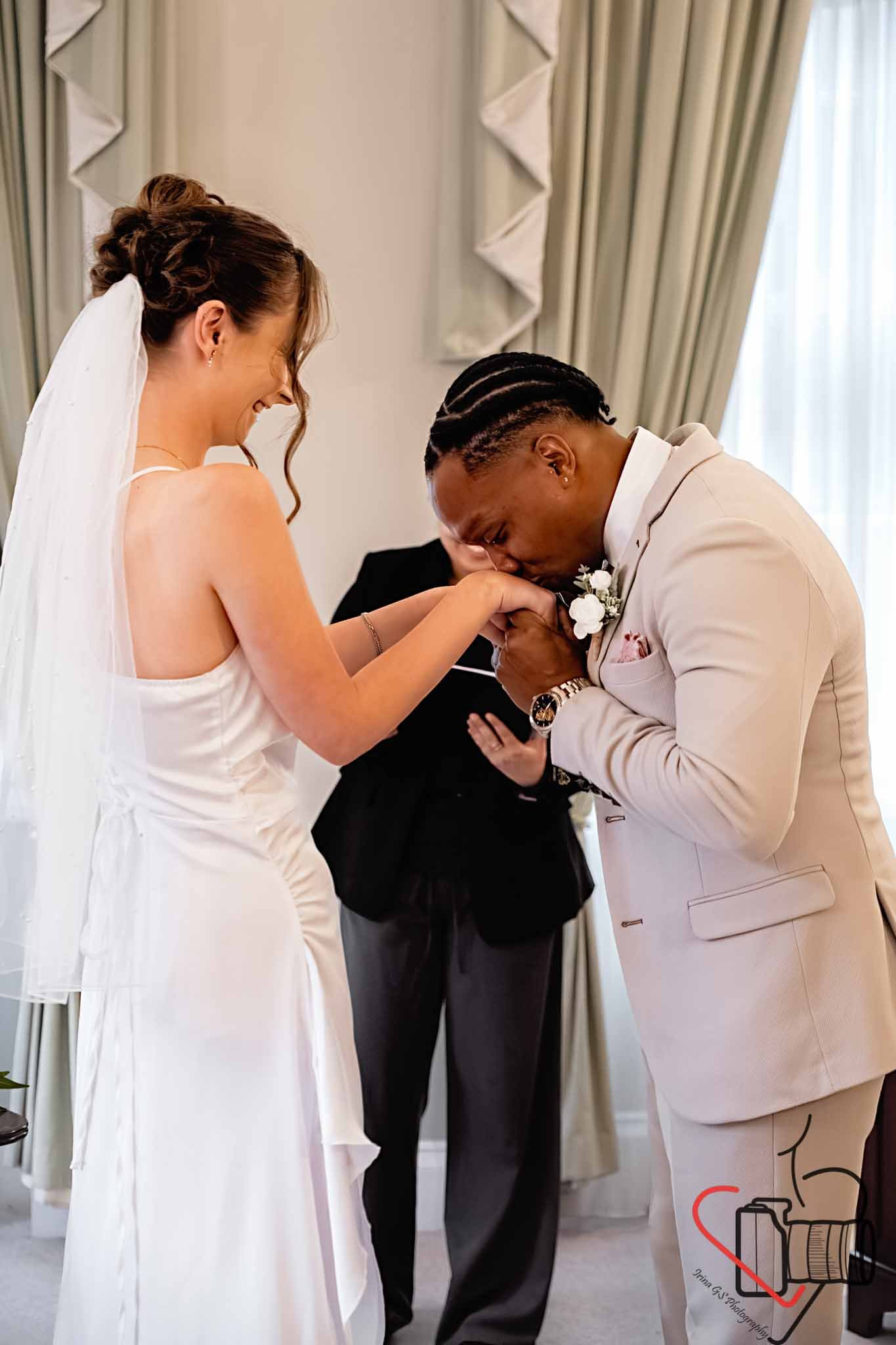 A bride and groom sharing a kiss, with the groom holding the bride's hand and kissing it during their wedding ceremony. Portsmouth Register Office, Milldam House.