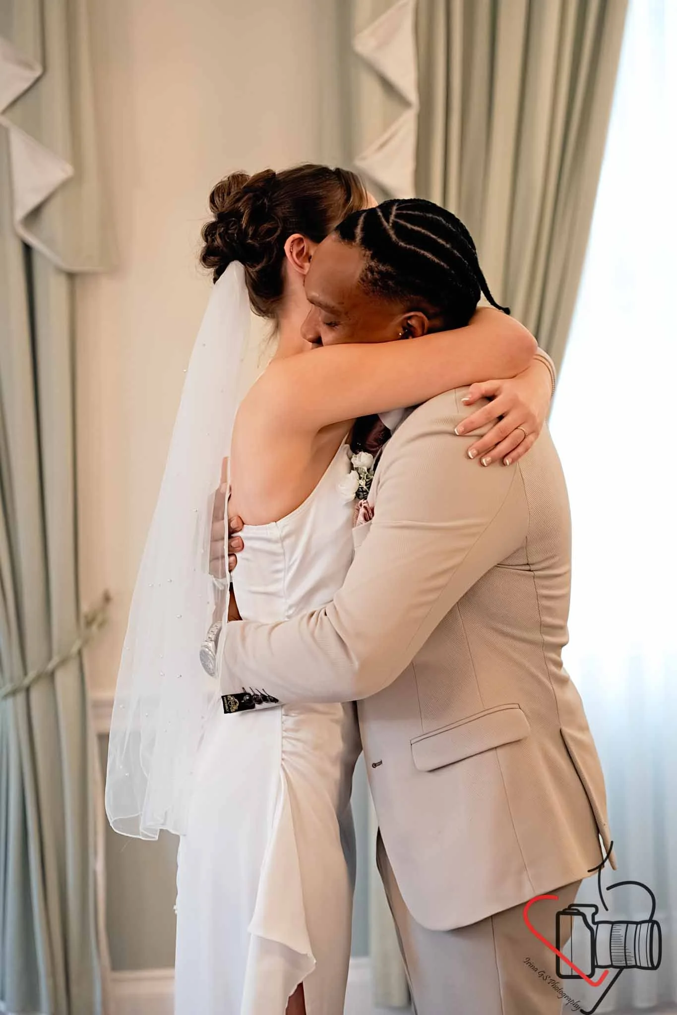 A bride and groom embrace during their wedding ceremony, with their eyes closed and happy expressions, in front of a backdrop of curtains. Portsmouth Register Office, Milldam House.