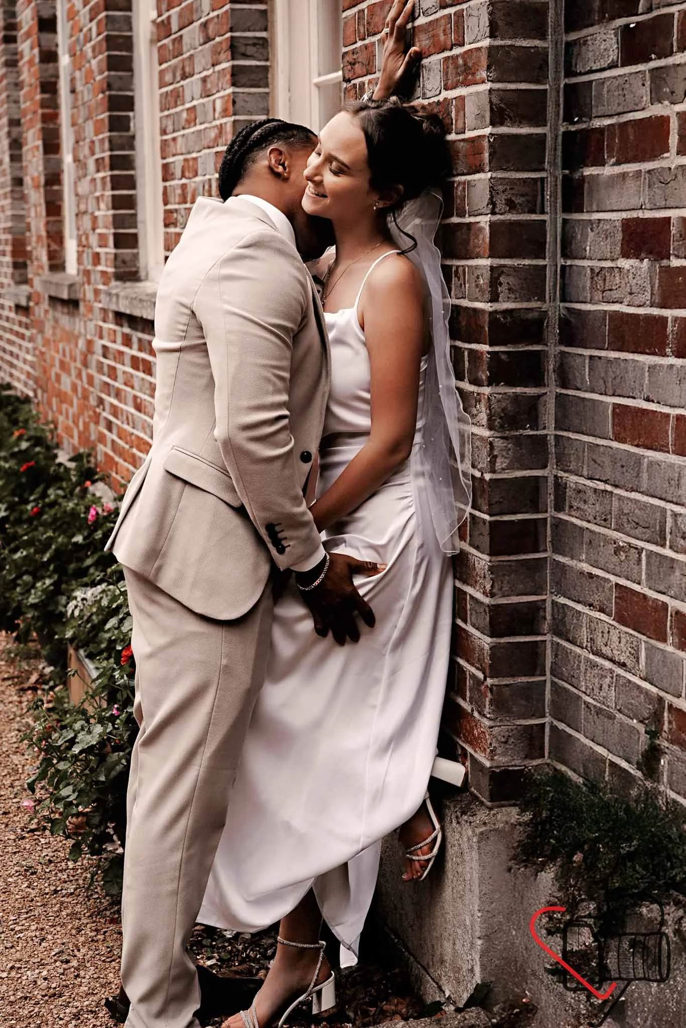 A couple dressed in wedding attire leaning against a brick wall, sharing an intimate moment and smiling. Portsmouth Register Office, Milldam House.