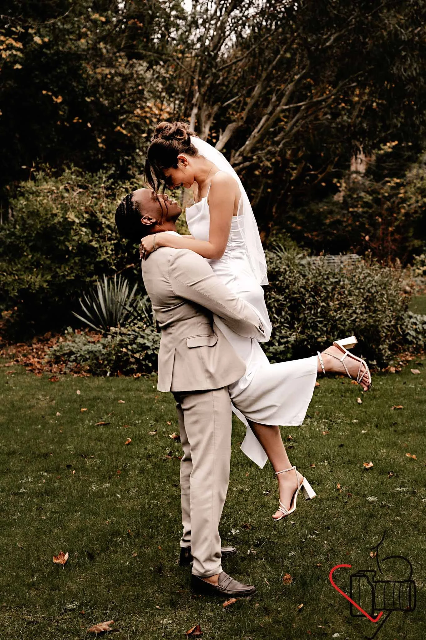 A couple dressed in wedding attire, with the man lifting the woman in a garden setting, surrounded by trees and greenery. Portsmouth Register Office, Milldam House.