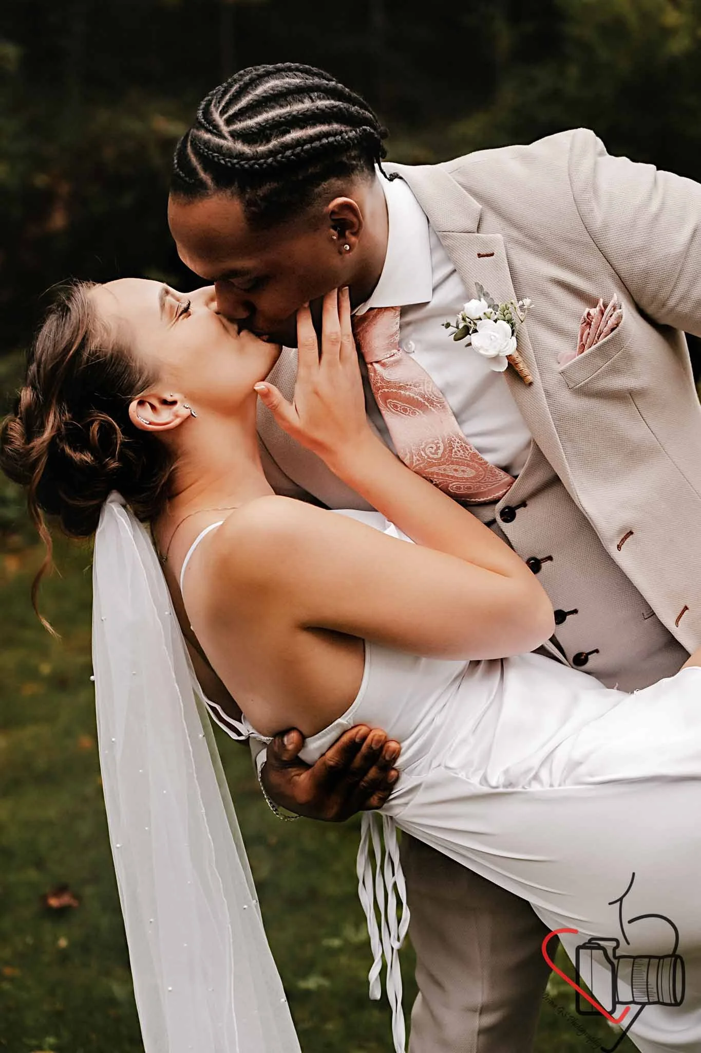 A newlywed couple sharing a kiss outdoors, with the groom gently holding the bride and the bride with her hand touching the groom's face. Portsmouth Register Office, Milldam House.