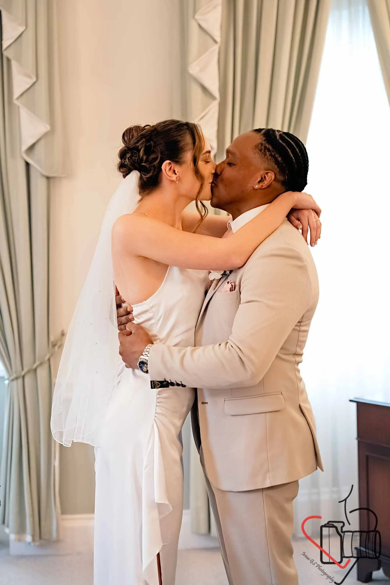 A bride and groom share a kiss in a room with elegant curtains. Portsmouth Register Office, Milldam House.
