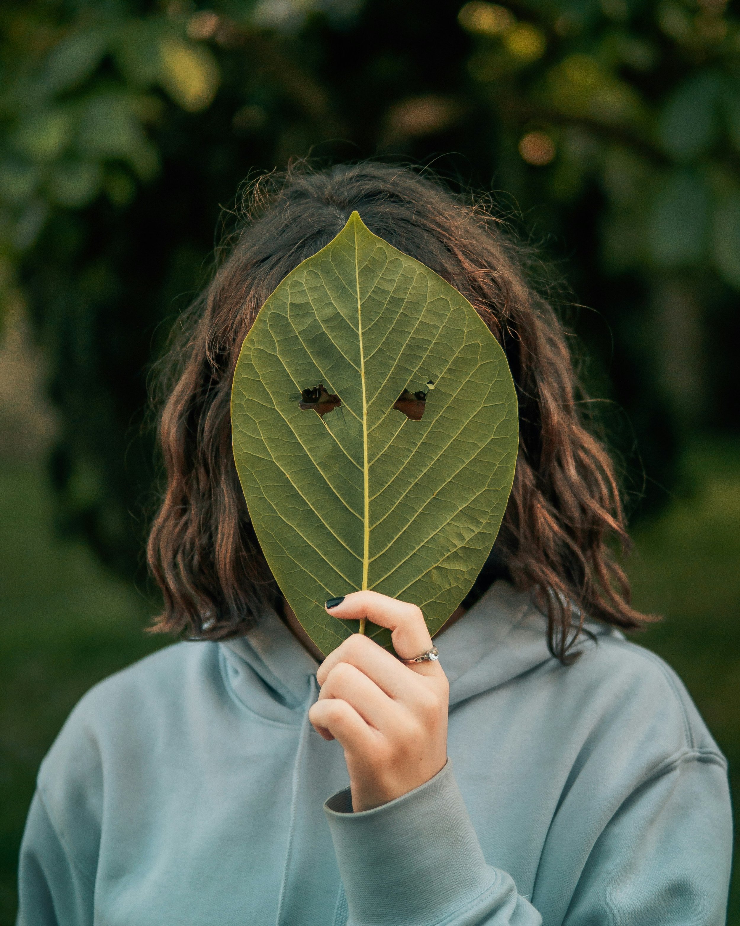 Woman holding leaf in front of her face to appear invisible