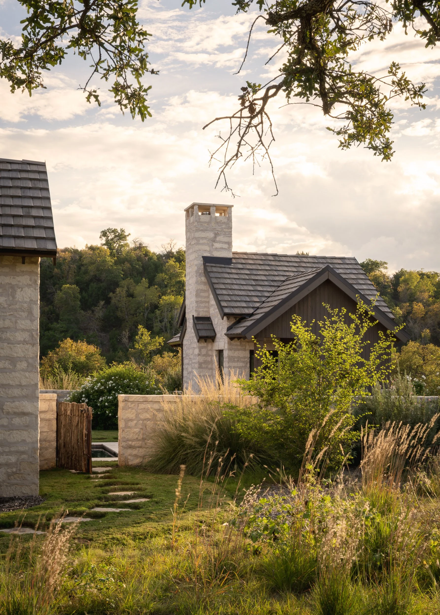 Sunset view of houses with stone chimneys, surrounded by greenery and trees, under a partly cloudy sky.