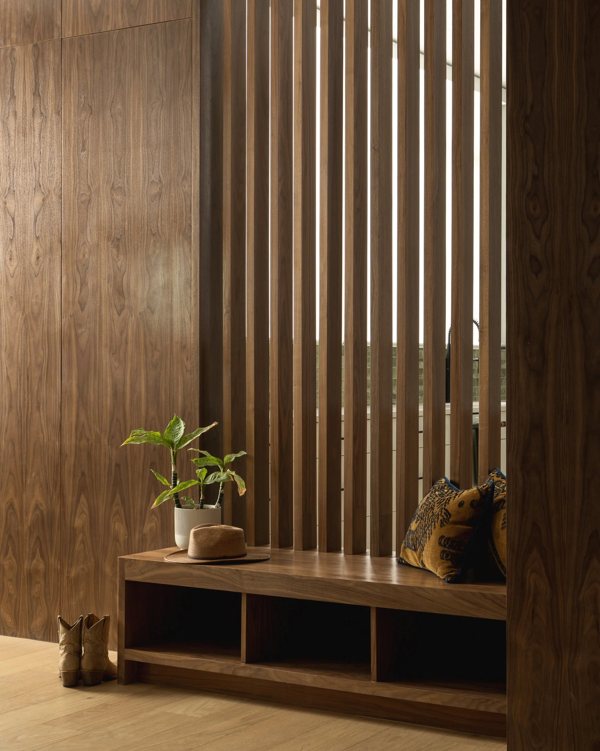 Interior space with a wooden wall, a wooden shelf, a potted plant, a straw hat, cowboy boots, and a leopard-patterned pillow.
