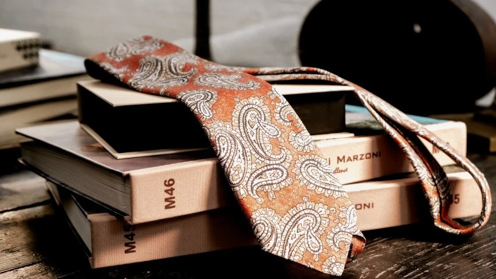 rust color paisley neck tie handmade in Italy on a stack of design books
