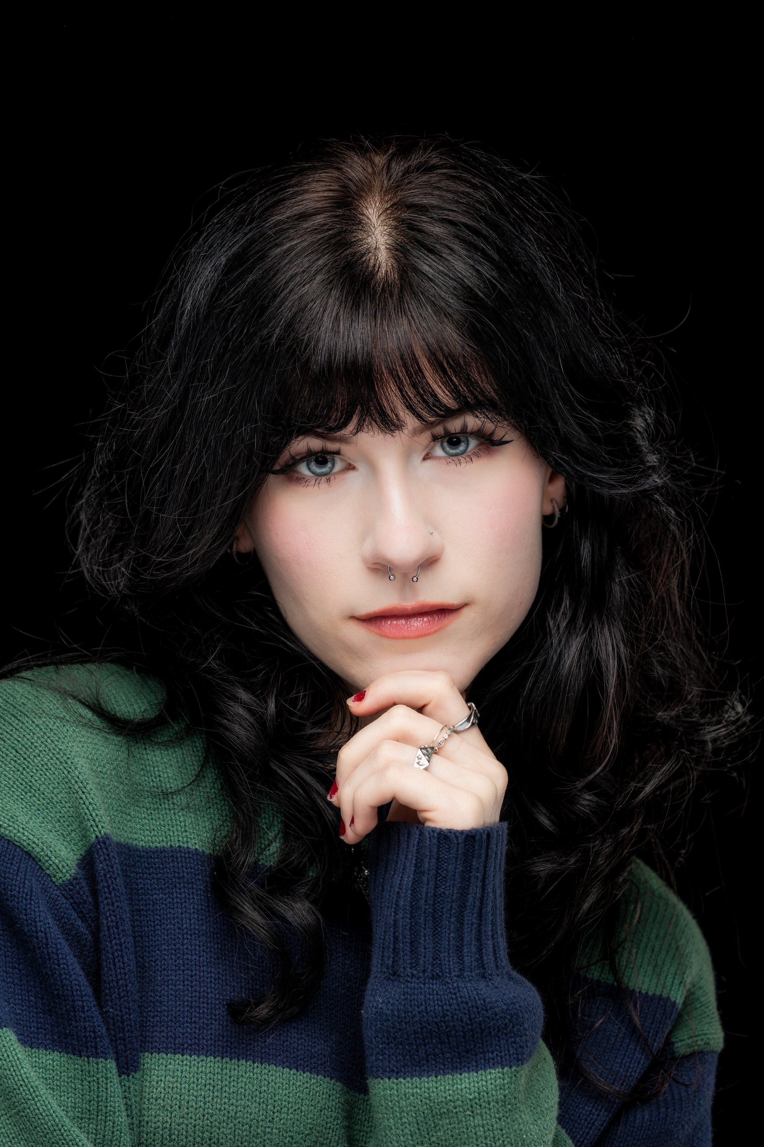 Studio portrait of a young woman in a green and navy striped sweater against a black background.