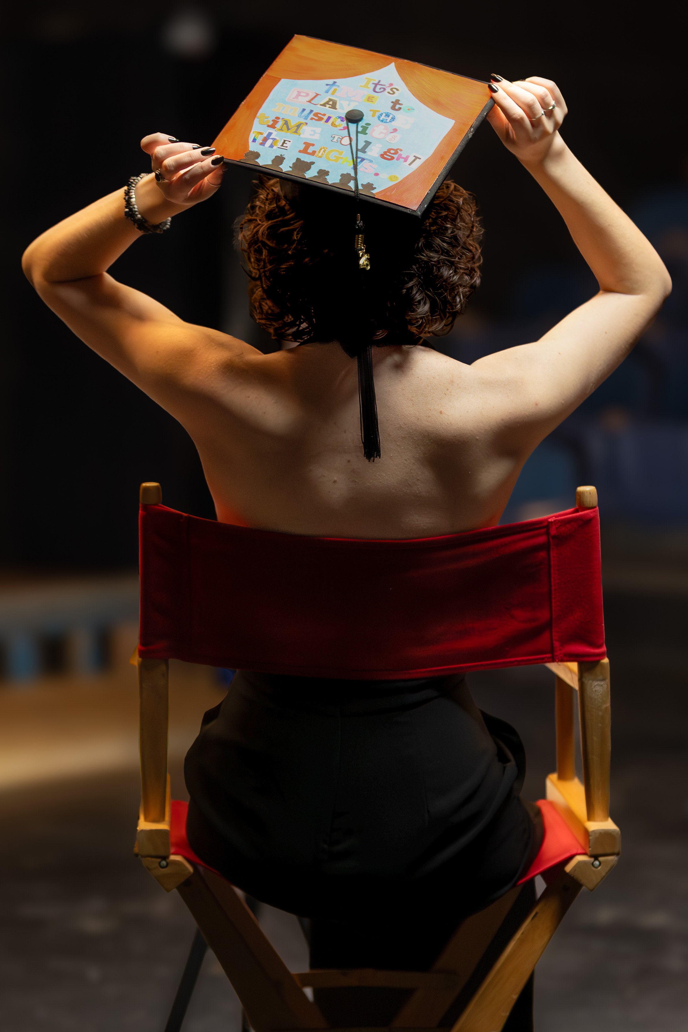 Creative senior portrait of a graduate holding a decorated graduation cap against a black background.