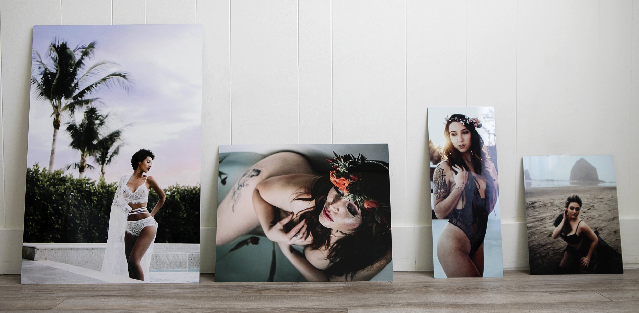 Four large photographic prints of women in various outdoor settings and poses, leaning against a white wall.