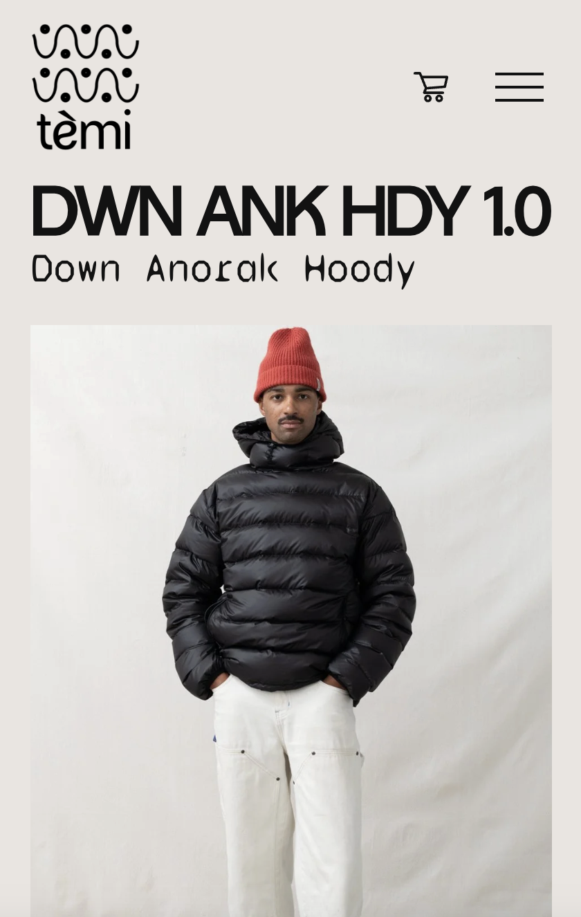 Man wearing a black down hoodie, white pants, and a red beanie standing against a white background.