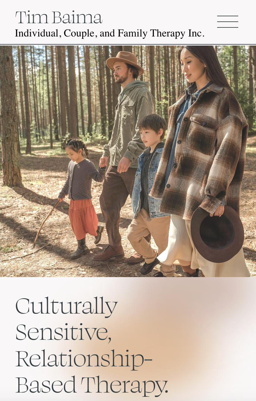 A family walking through a forest, holding hands. The family includes a man with a beard, wearing a hat and striped shirt; a woman in a plaid jacket holding a hat; a young boy in a denim jacket; and a young girl with braids wearing a sweater and skirt.