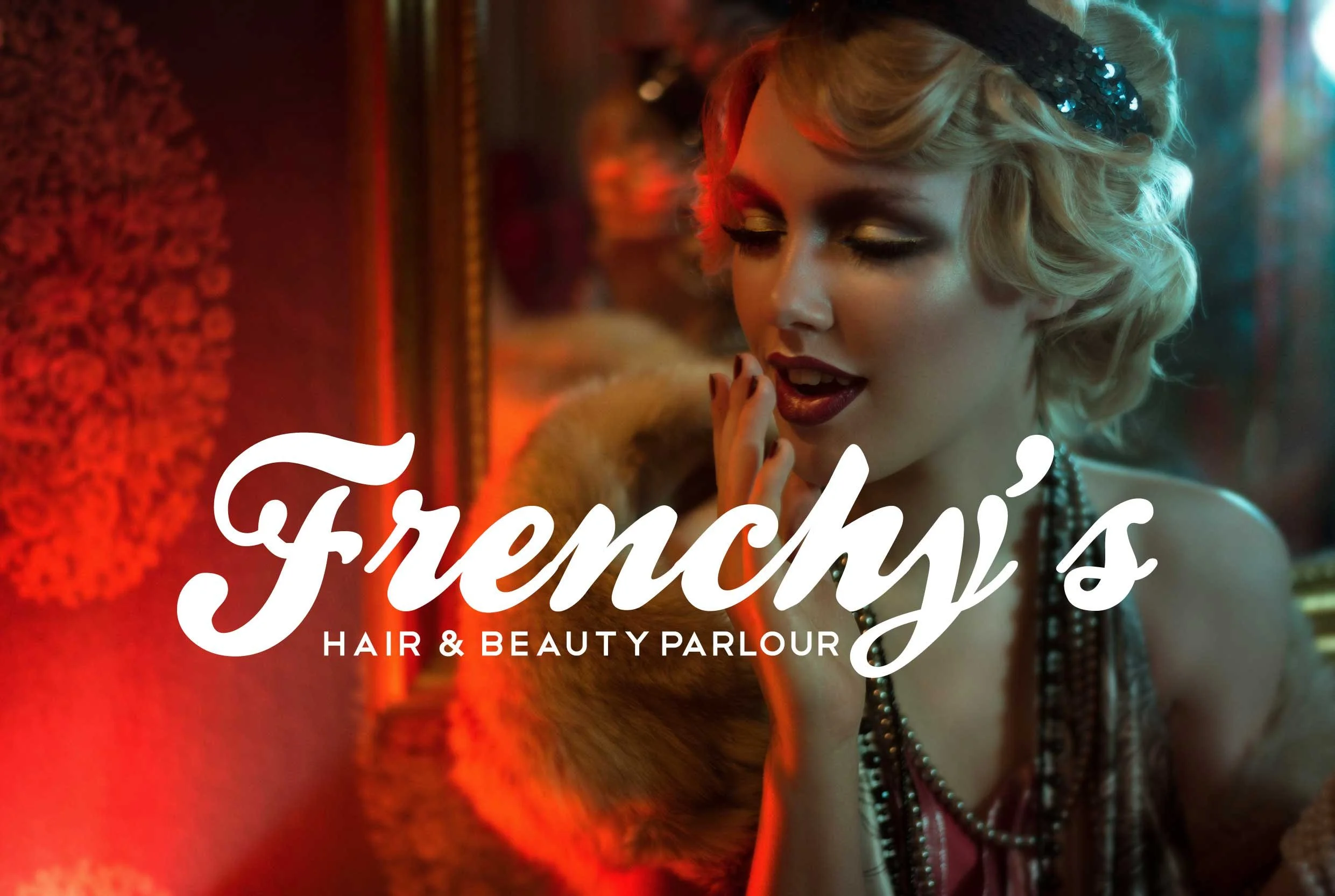 A woman with blonde hair styled in vintage waves, wearing a black headband with sequins, appears to be applying makeup or preparing herself at a hair and beauty parlor. The background has warm red and orange lighting with decorated walls.
