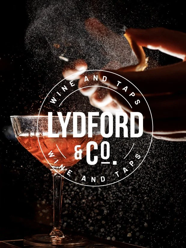 A person is pouring red wine into a glass with a splash, with the logo 'Lydford & Co. Wine and Taps' overlayed in white text.