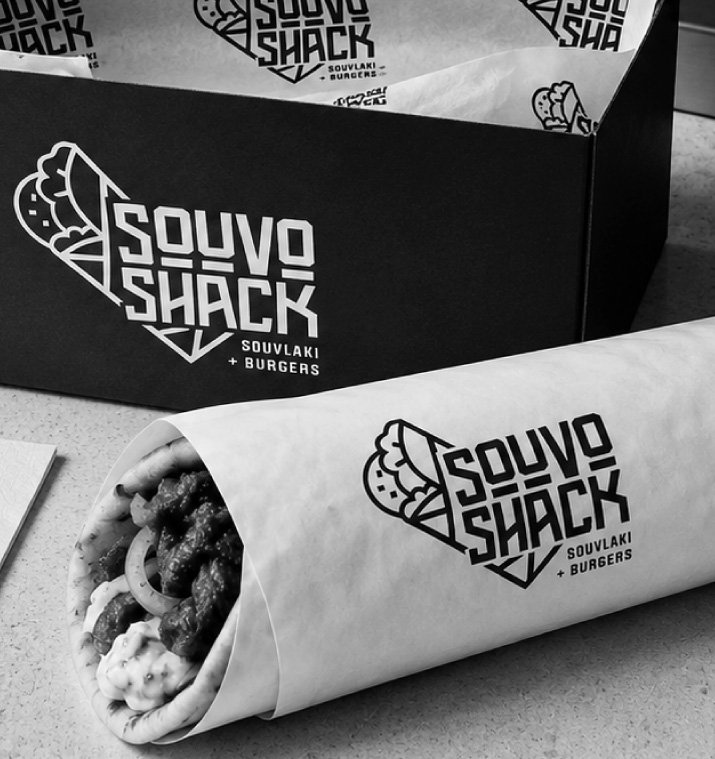 A takeout container and paper wrap from Souv Shack, a restaurant selling souvlaki and burgers, on a table.