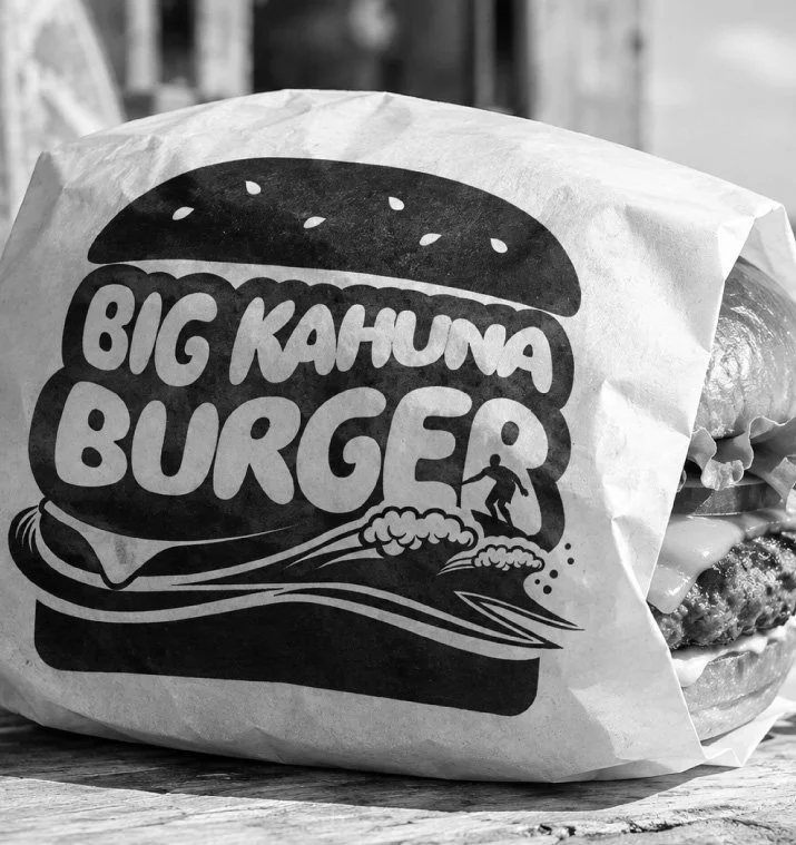 A wrapped burger from Big Kahuna Burger with a logo depicting a burger and a surfer riding a wave.