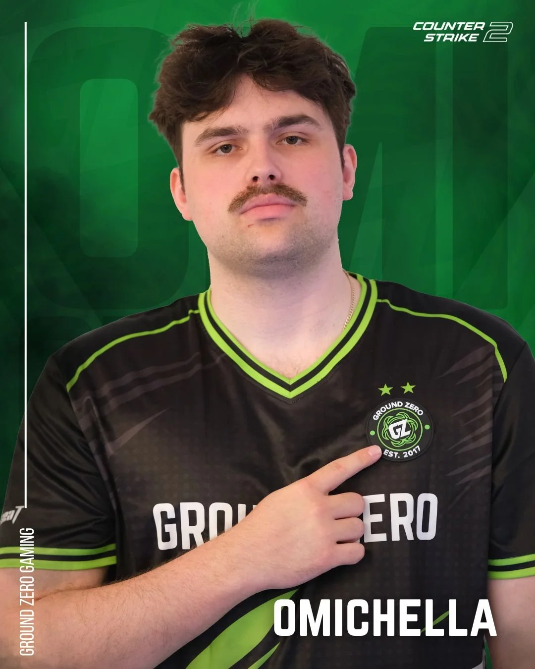 Young man with curly brown hair, mustache, wearing a black and green esports jersey with Ground Zero logo, pointing to the logo on his chest, against a green background with Counter-Strike 2 branding.