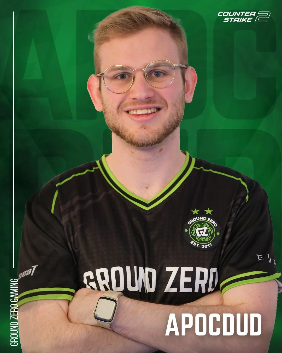 A young man with glasses and a beard wearing a black gaming jersey with green accents, standing with arms crossed against a green background. The jersey has the Ground Zero Gaming logo and the words "GROUD ZERO" on it. Text on the image includes "Counter Strike 2" in the upper right corner and "APOCDUD" at the bottom.