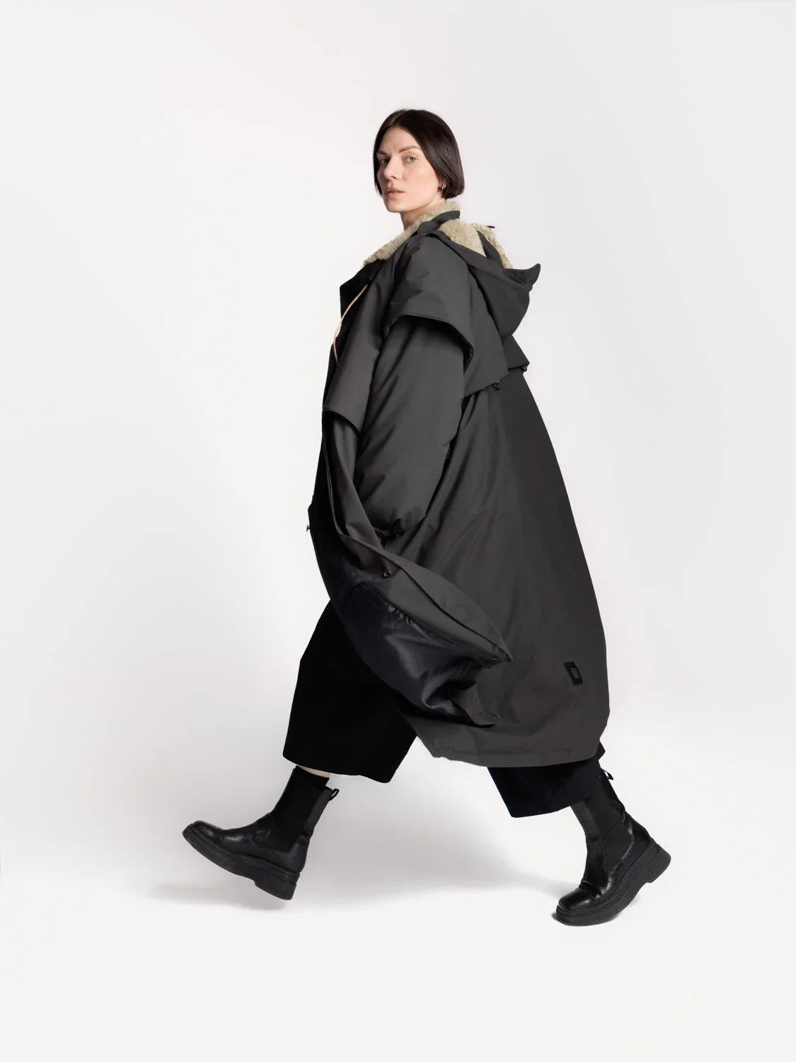 En kvinne iført en stor svart olivendel nedenfra og opp.