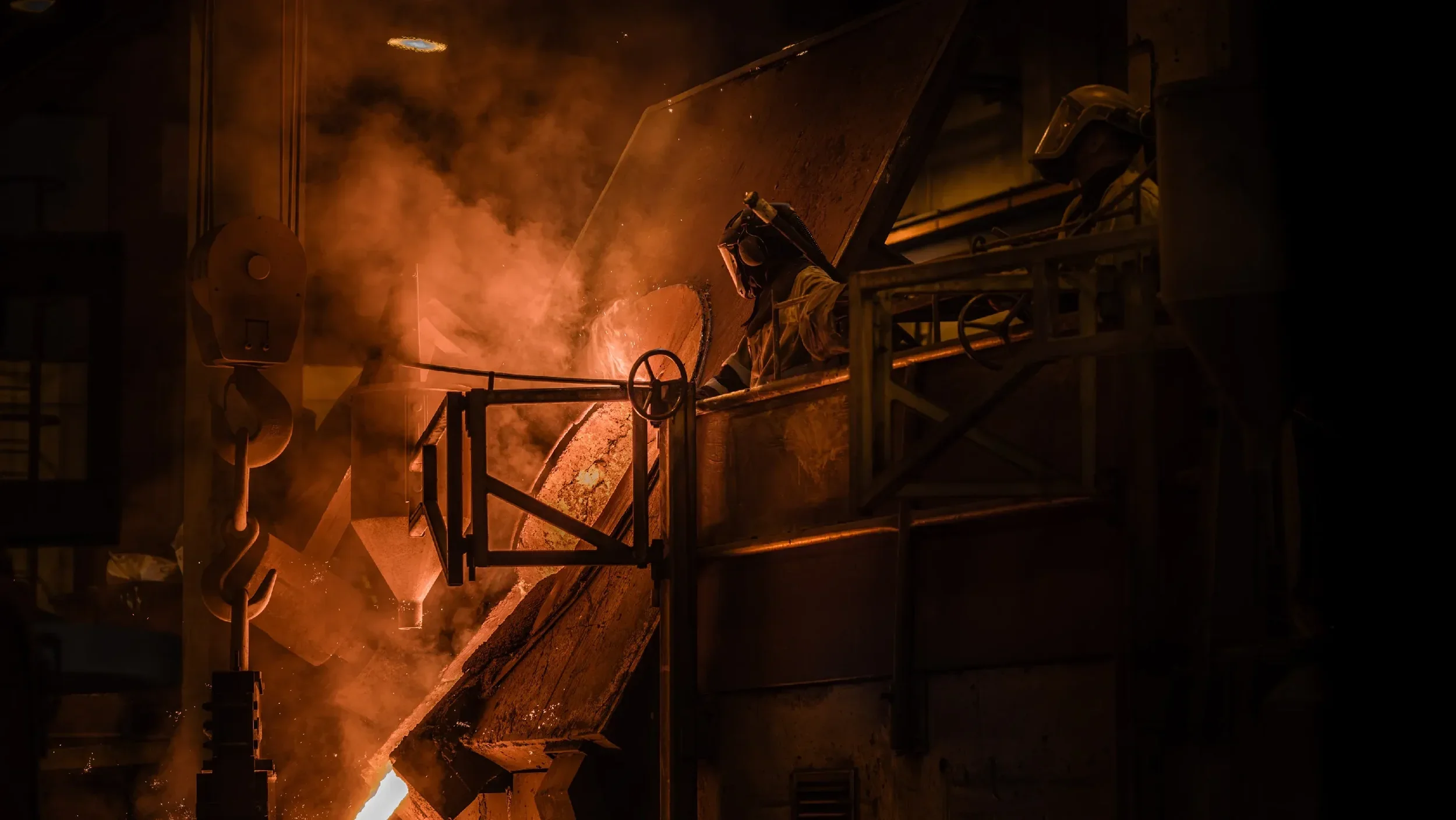 En verktøymaskin som smelter metall ved høye temperaturer med en person som overvåker prosessen. Resultatet er en lysende, varm og skiftende farget lampe i en industribedrift.