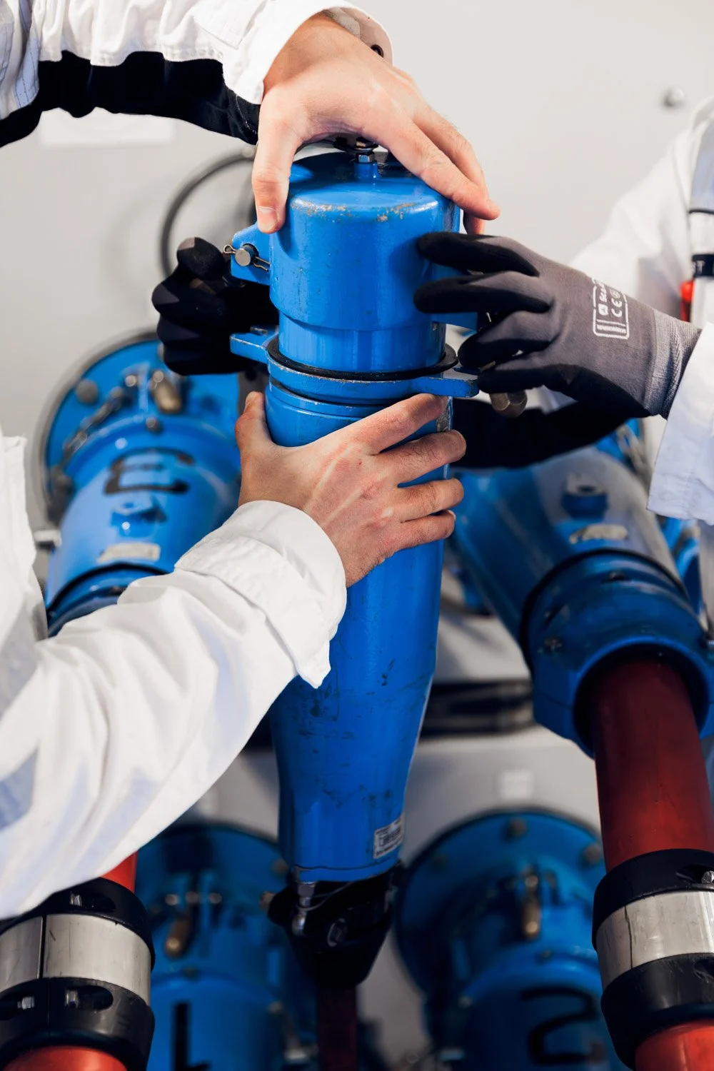 To personer jobber med å installere eller vedlikeholde en blå vannpumpe med rør og koblinger.