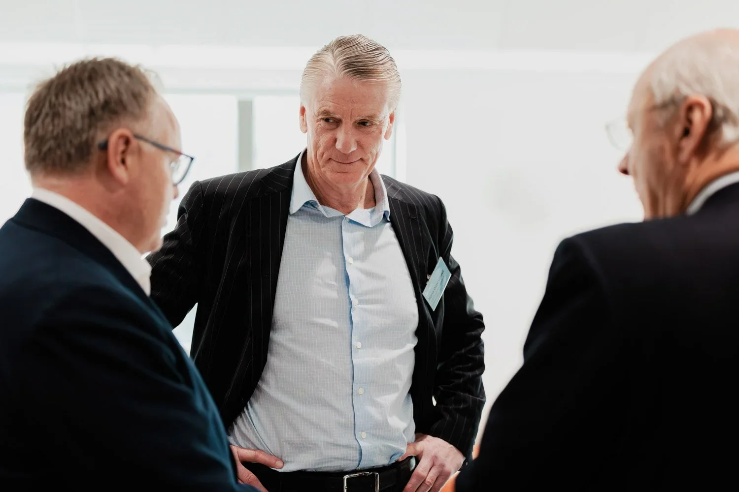 Tre voksne menn i formelle klær har en samtale på et kontor.
