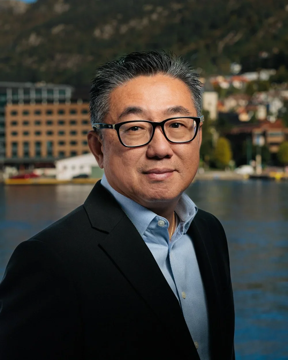 Portrett av en teknologileder foran en bygd med vann og fjell i bakgrunnen.