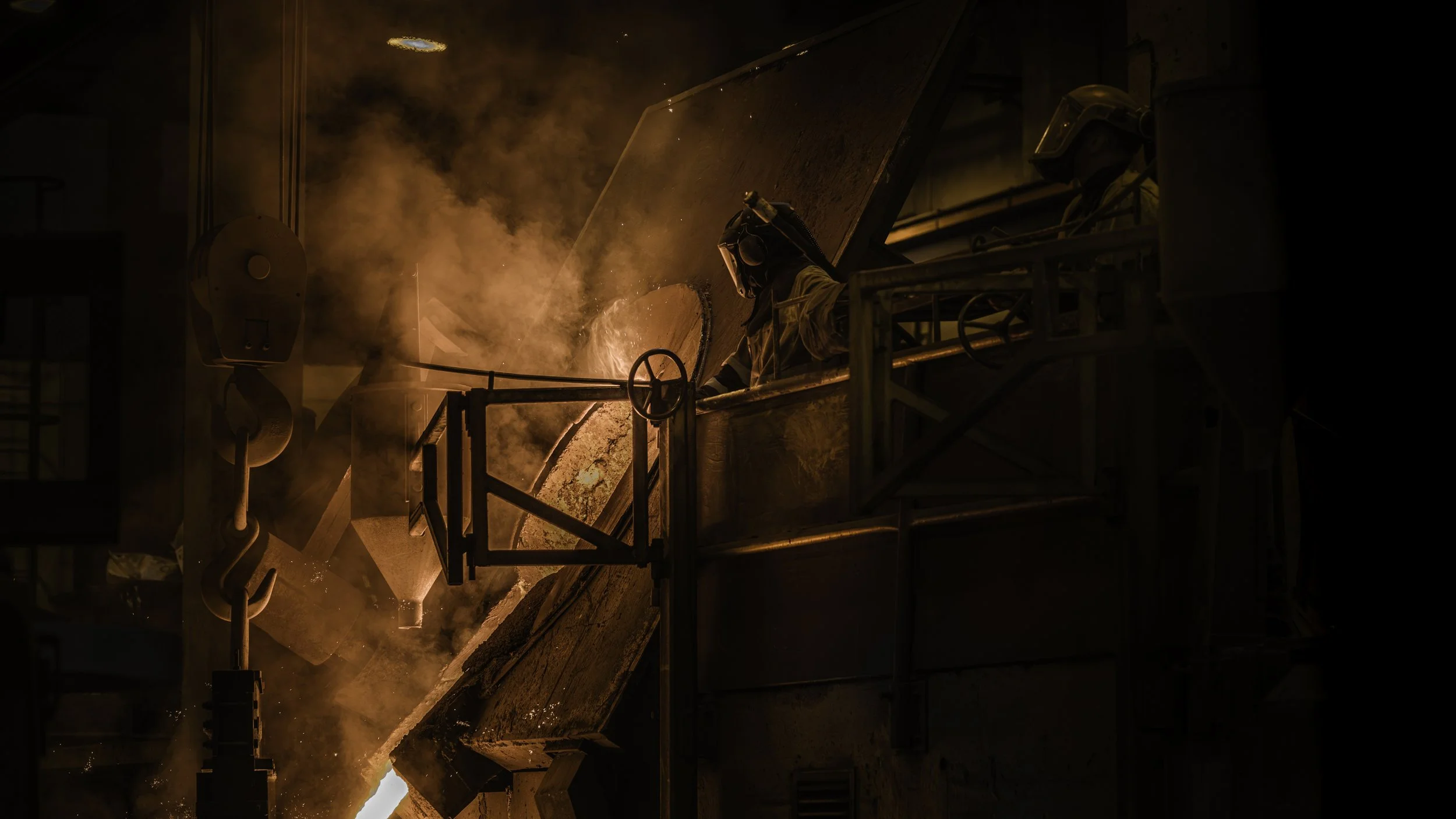 En sveisende person arbeider i en industriell setting med den orange-glødende smeltede metallen og røyk rundt seg.