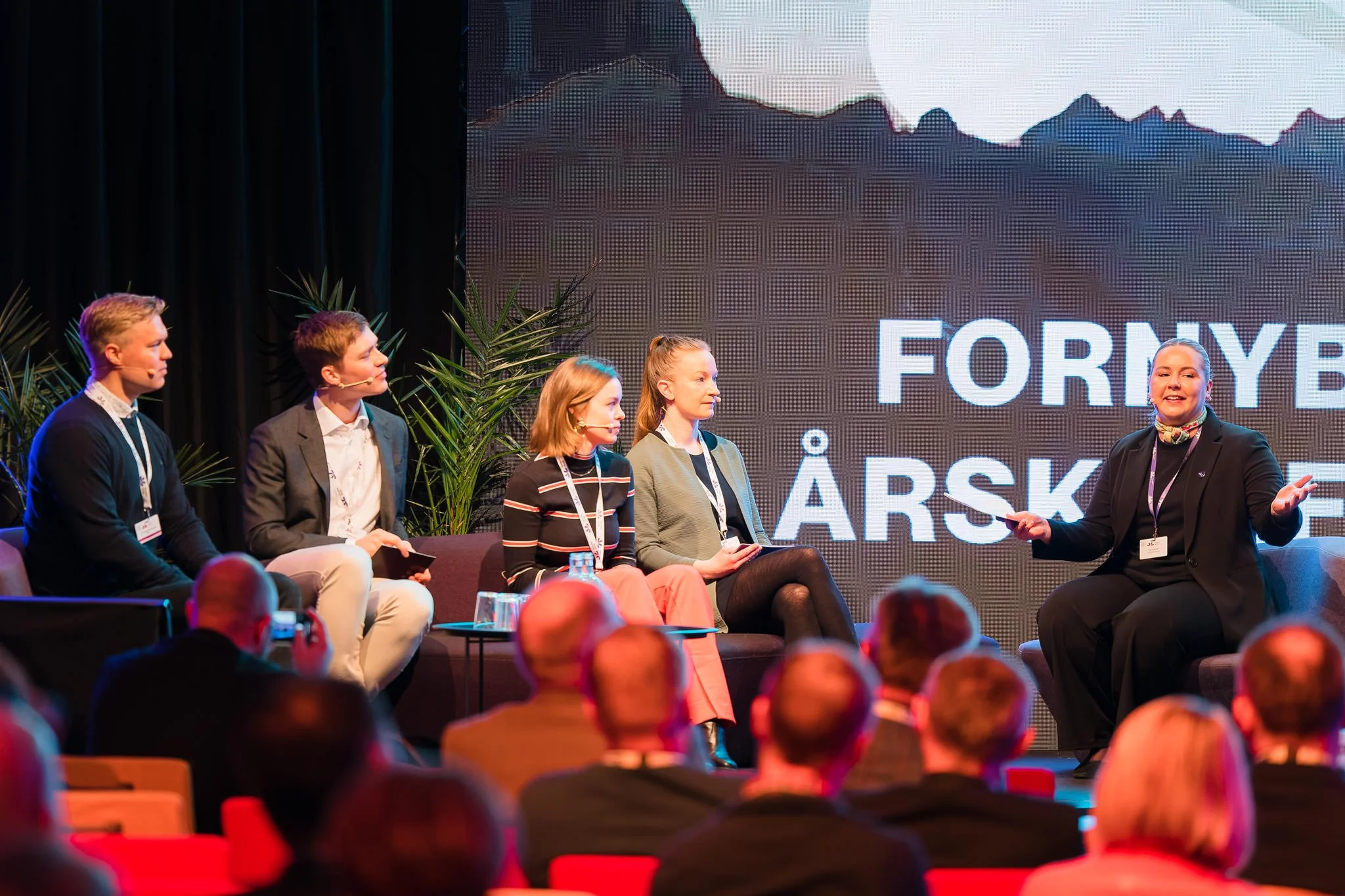 En panel med fem personer som deltar i en diskusjon på en scene foran et publikum. Bak scenen er det en stor skjerm med teksten "FREM» og noe mer tekst. Paneldeltakerne snakker og ser engasjerte ut, og publikum lytter oppmerksomme.