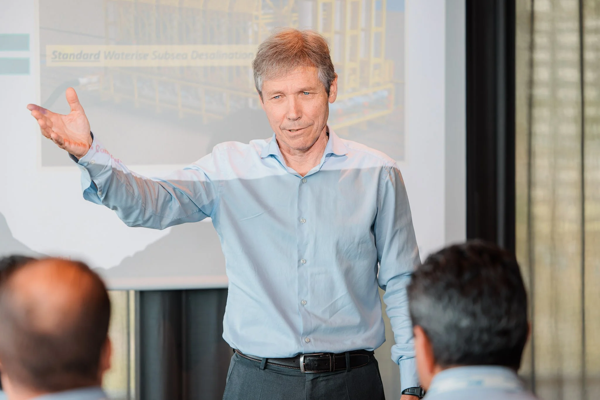 En mann som holder en presentasjon foran en gruppe mennesker i et konferanserom.