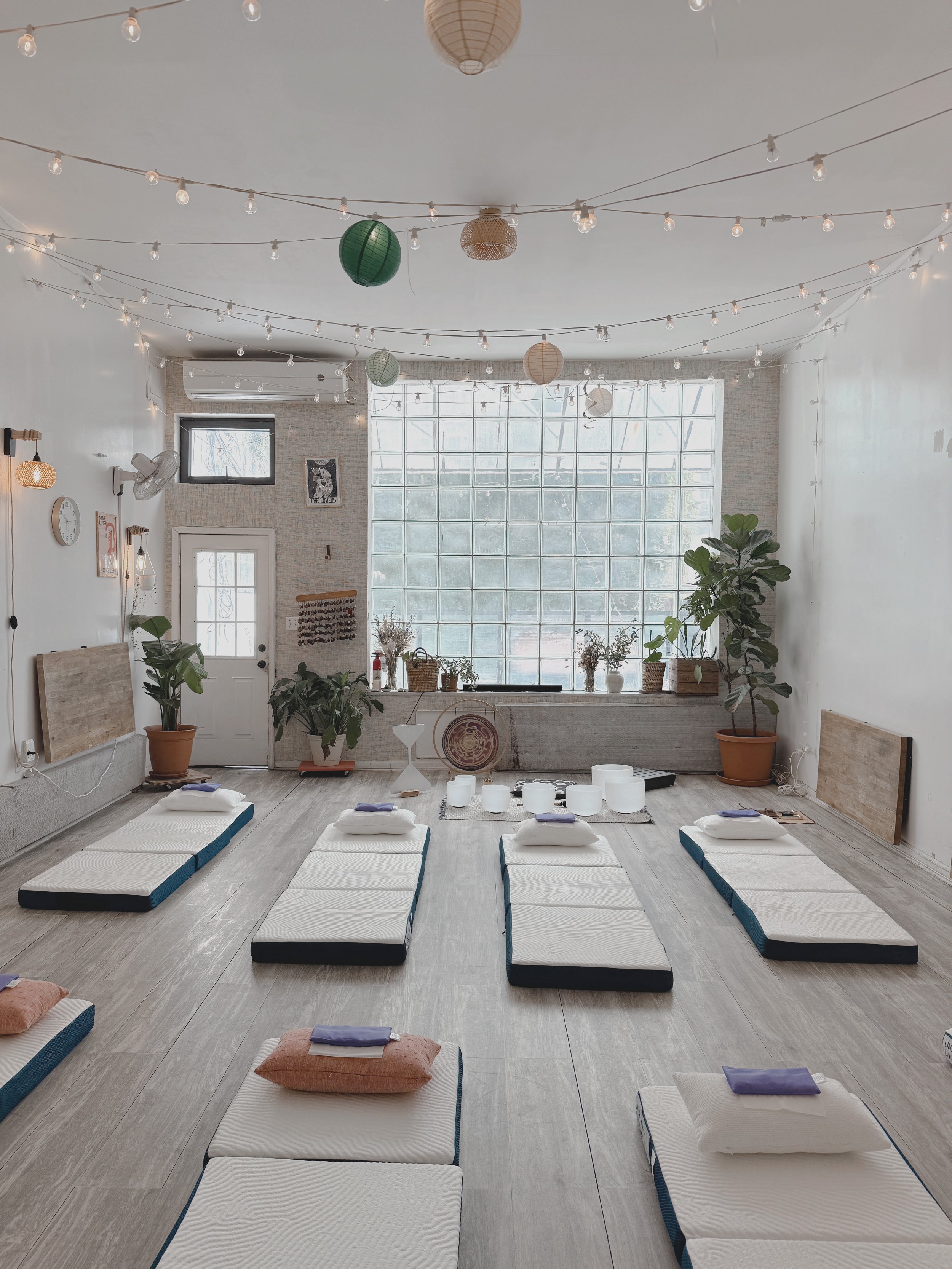 Soundawn's private sound bath studio in Williamsburg, Brooklyn — cushioned mats, crystal singing bowls, and warm string lights set up for an in-studio session.